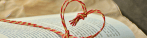 Picture of a book with a strand of twine stretched across the open pages. The twine is tied in the shape of a heart that stands up with it's point at the crease of the pages.